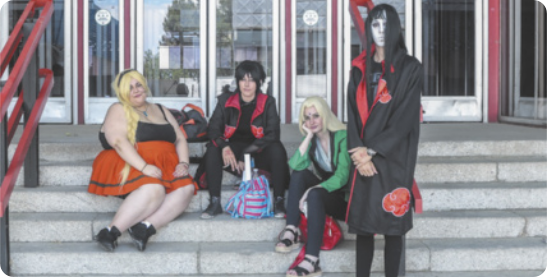 Fotografia de quatro jovens sentados em uma escadaria em frente a um portão. Eles estão fantasiados de diferentes personagens de desenhos animados japoneses.