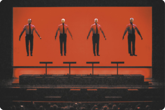 Fotografia de Ralf Hütter, Fritz Hilpert, Henning Schmitz e Falk Grieffenhagen: quatro músicos em um palco, integrando o grupo Kraftwerk. As imagens deles aparecem em uma tela no palco, flutuando sobre um pano de fundo vermelho, usando camisas e gravatas, com os corpos eretos e os braços abertos ao lado do corpo.