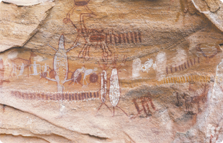 Fotografia de uma parede rochosa com pinturas de figuras humanas e animais diversos, além de grafismos verticais enfileirados.