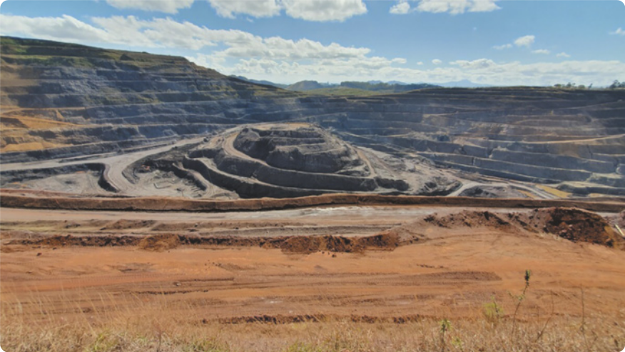 Fotografia de uma paisagem montanhosa degradada e desmatada pela mineração, com o relevo reduzido a patamares por onde circulam pequenas estradas de terra.