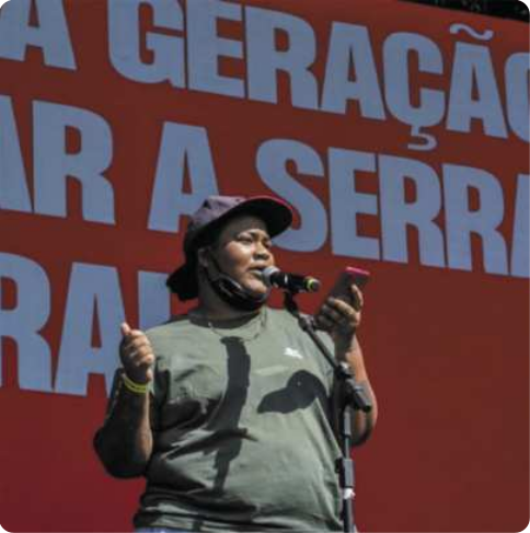 Fotografia de Nilo Nūhatê Ybyraporãuma. Ele é um homem indígena de boné falando diante de um microfone, com um smartphone na mão.