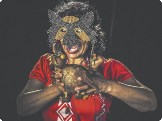 Fotografia de Alicce Oliveira: uma mulher com um boneco de cabaça nas mãos, usando uma máscara.