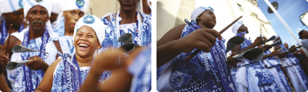 Duas fotografias mostrando um grupo de pessoas uniformizadas e enfileiradas, usando lenços na cabeça, roupas brancas e faixas no pescoço, tocando instrumentos de percussão. Entre eles há pessoas idosas e jovens.