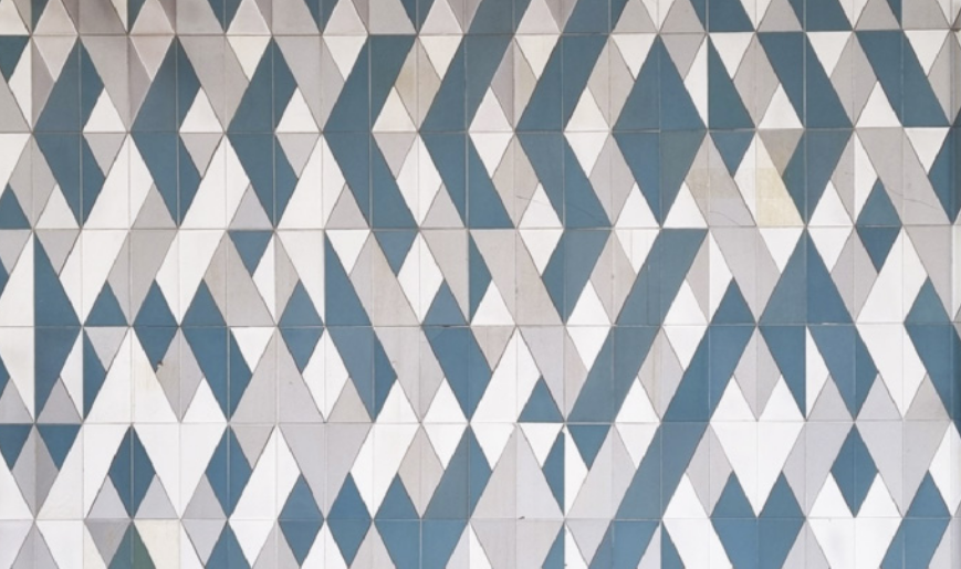 Fotografia de painel com mosaico de triângulos e losangos dispostos em uma grade regular geometrizada. Porém, a composição do mosaico articula peças de três cores, de modo irregular, configurando uma articulação de figuras, planos e formas geométricas diversas que promovem a sensação de profundidade e dinamicidade ao painel.