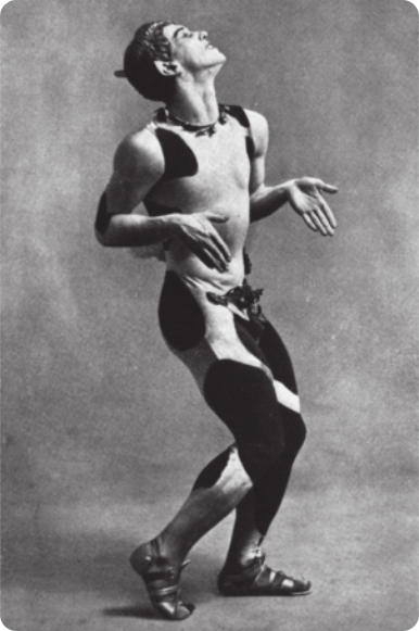 Fotografia em preto e branco de Vaslav Nijinsky: um bailarino vestido com roupas coladas ao corpo, com manchas pretas. Ele está em pé, com as pernas levemente flexionadas, erguendo um dos calcanhares. Ele está olhando para cima, com os braços flexionados junto ao corpo, e as mãos abertas voltadas para baixo.