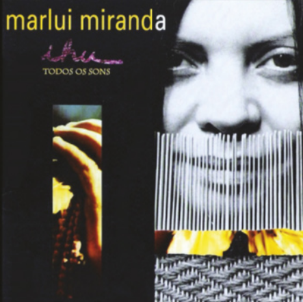 Capa de álbum com composição de imagens: há a fotografia em preto e branco do rosto de uma mulher com varetas à frente da boca; um detalhe de cesta de palha trançada; e a mão de uma pessoa segurando um colar de contas.