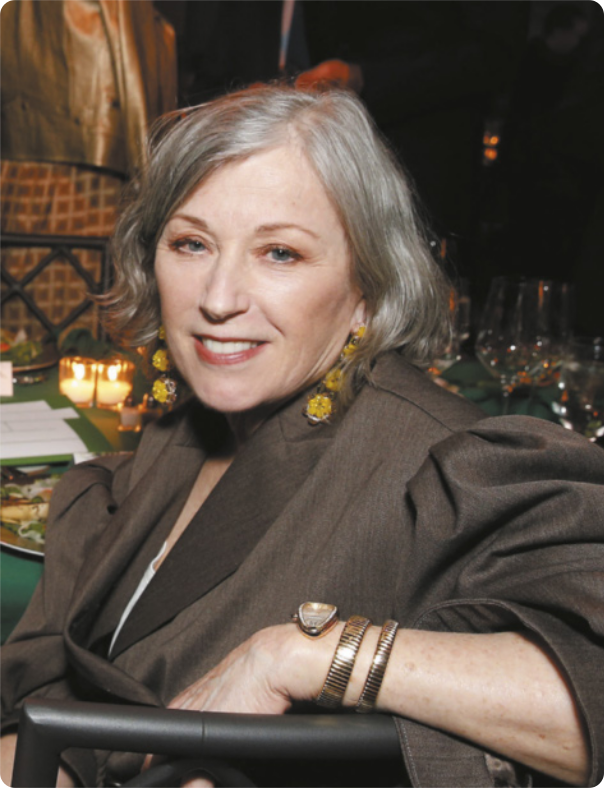 Fotografia de Cindy Sherman. Ela é uma mulher de cabelos grisalhos, usando brincos e pulseiras, vestida com uma espécie de paletó.