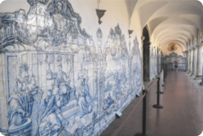 Fotografia de uma parede em um corredor de convento, coberta por um painel de azulejos com pinturas na cor azul, representando figuras e cenas bíblicas e ornamentos barrocos.