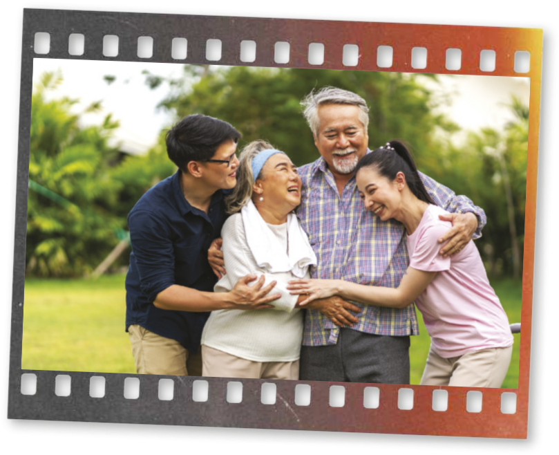 Fotografia de uma família se abraçando ao ar livre. Há um casal mais velho e um homem e uma mulher mais novos.