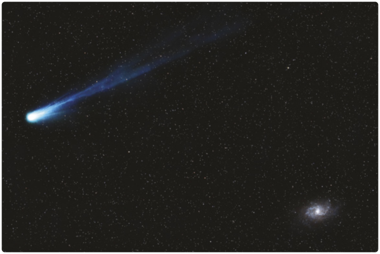 Imagem de um cometa no espaço. O cometa tem uma ponta arredondada e brilhante, possui uma cauda luminosa e longa. No canto inferior direito, há um corpo celeste brilhante indefinido. Em segundo plano, estão inúmeras pequenas estrelas.