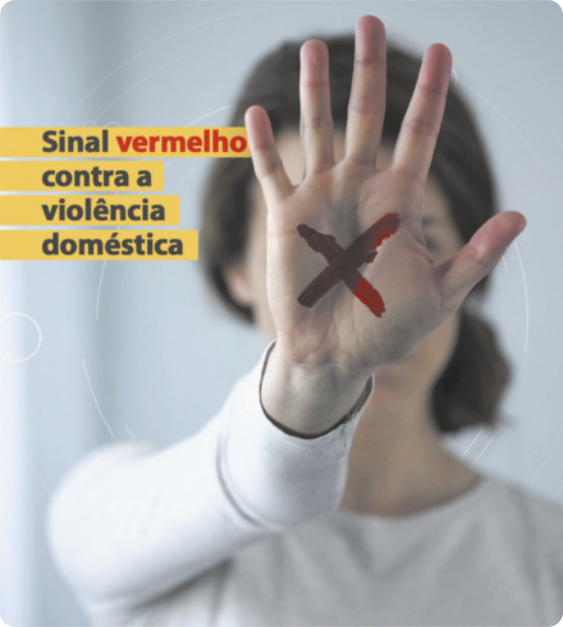Cartaz de uma mulher com o braço estendido, a palma da mão aberta e os dedos voltados para cima, de forma que a mão cobre seu rosto. Na palma da mão há um X desenhado. Ao lado da mão está escrito 'Sinal vermelho contra violência doméstica'.
