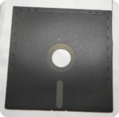 Fotografia de disquete, um objeto de plástico com formato quadrangular, com um furo no centro e pequenas partes em metal.