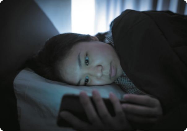 Imagem de mulher deitada na cama usando celular.