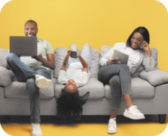 Imagem de homem, criança e mulher sentados no sofá, utilizando notebook, celular e tablet.