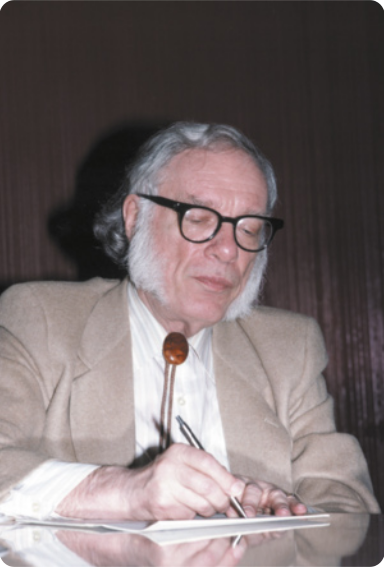 Fotografia de Isaac Asimov. Ele é um homem branco, de cabelos e barba brancos, usa óculos e está escrevendo em um papel.