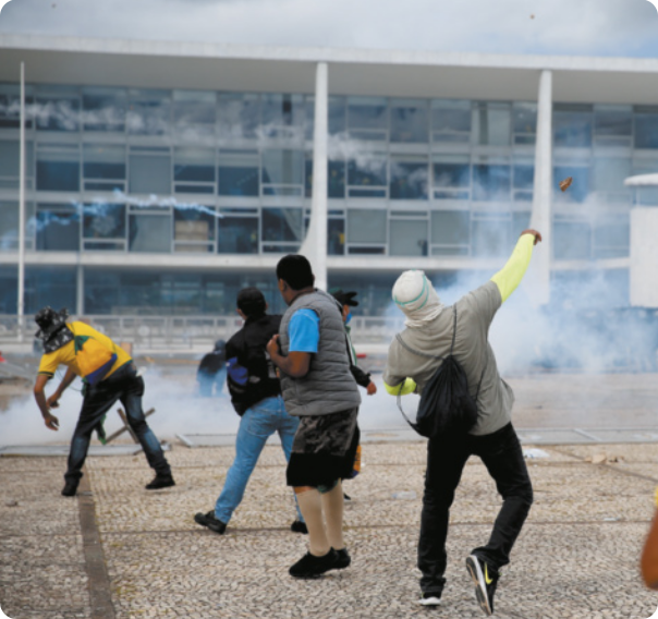 Fotografia de manifestantes jogando bombas em frente ao Palácio do Planalto.