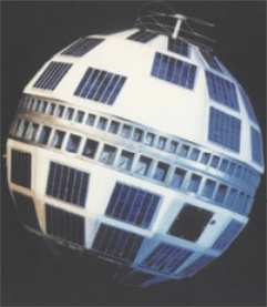 Imagem do satélite Telstar 1. Ele tem formato esférico com muitas placas na superfície.