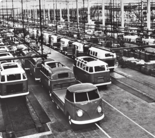 Fotografia em preto e branco de automóveis sendo montados em fábrica.