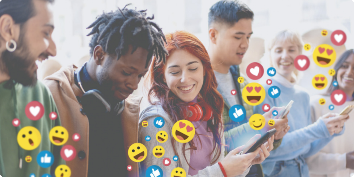 Imagem de pessoas jovens sorrindo e utilizando seus smartphones. Estão representados diversos emojis saindo dos smartphones.