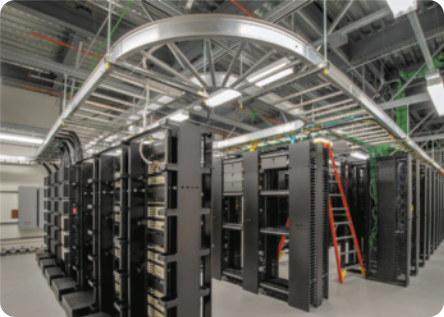 Fotografia de um data center. Há muitas fileiras de prateleiras com os equipamentos eletrônicos em um galpão.