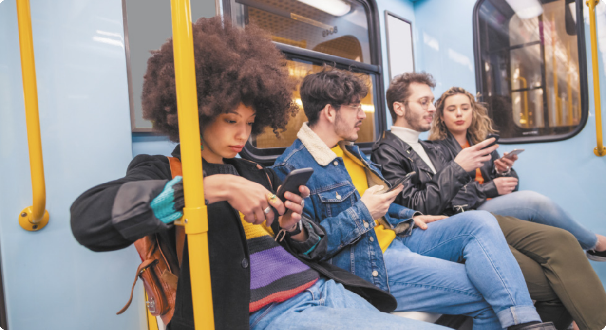 Imagem de pessoas sentadas em banco de transporte público, todos usando seus celulares.