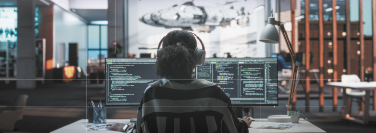 Fotografia de mulher olhando para dois monitores de computador em um escritório.