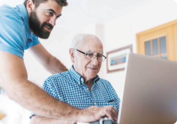 Imagem de um homem ajudando um senhor idoso a mexer em computador.