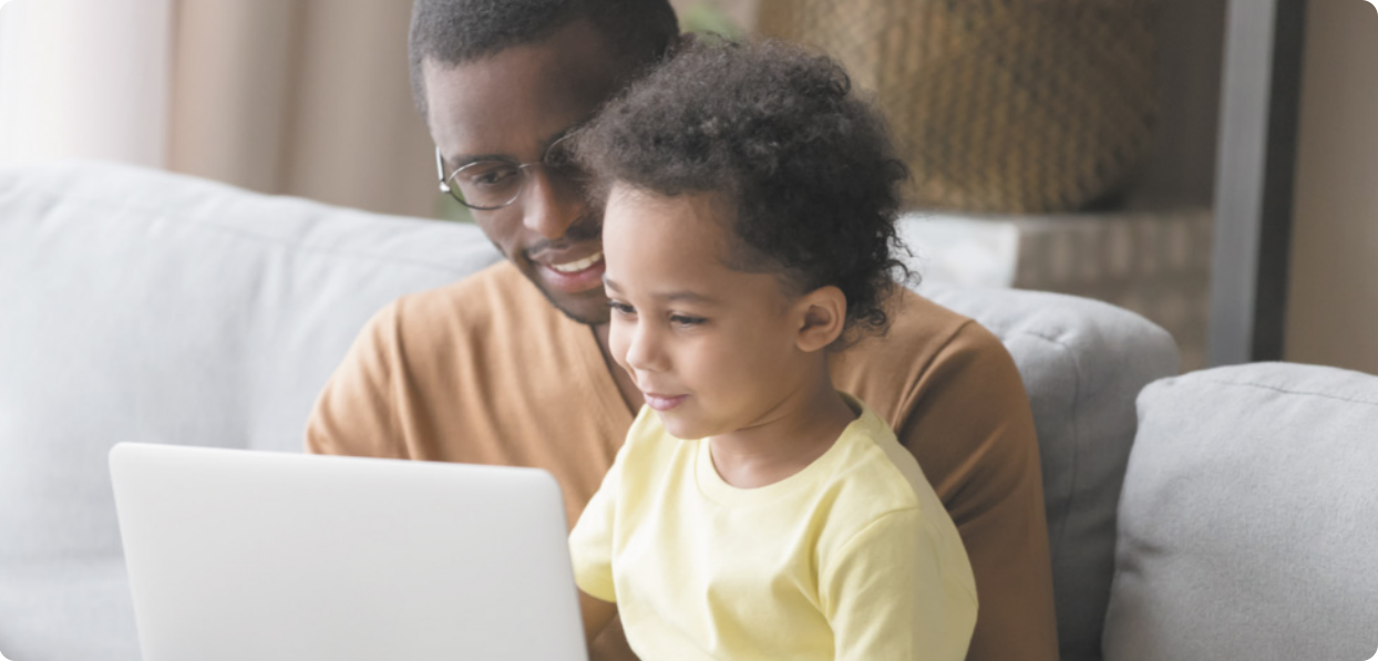 Fotografia de pai e filho sentados em sofá olhando para a tela de notebook.