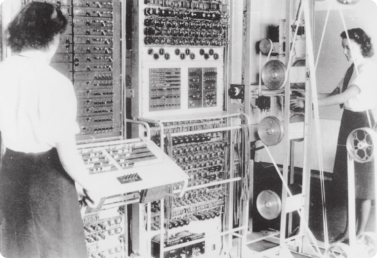 Fotografia em preto e branco de duas mulheres operando um grande computador.
