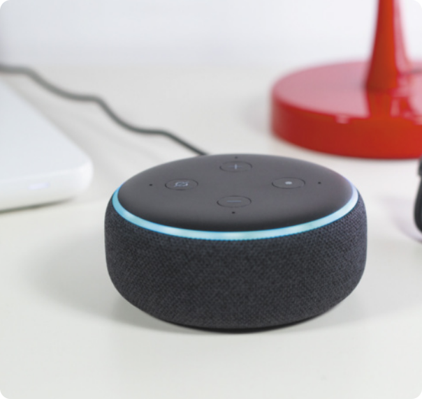 Imagem de assistente virtual sobre uma mesa; é um aparelho pequeno e cilíndrico com falantes e botões.
