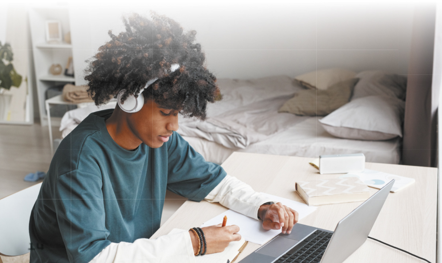 Imagem de jovem fazendo notações e utilizando computador em um quarto.