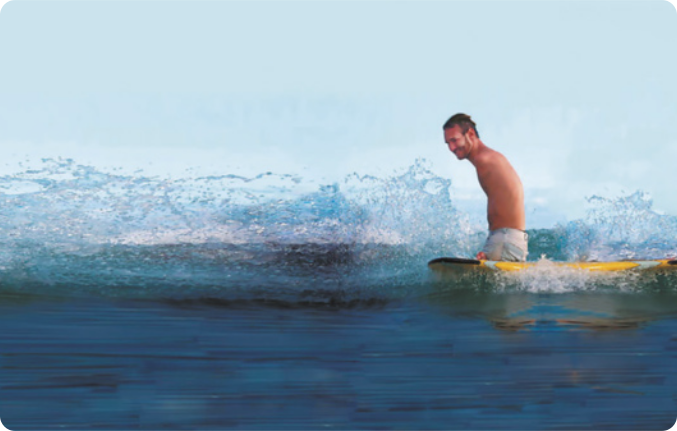 Fotografia de Nick Vujicic. Ele é um homem de cabelos curtos, sem camiseta, parcialmente imerso no mar, segurando uma prancha de surfe flutuando sobre a água.