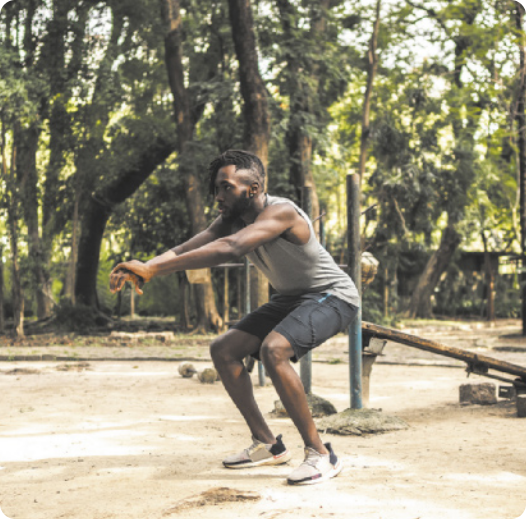 Fotografia de um homem em um parque, com os pés paralelos e os joelhos flexionados, inclinando o tronco para a frente, com os braços estendidos à frente e as mãos unidas.