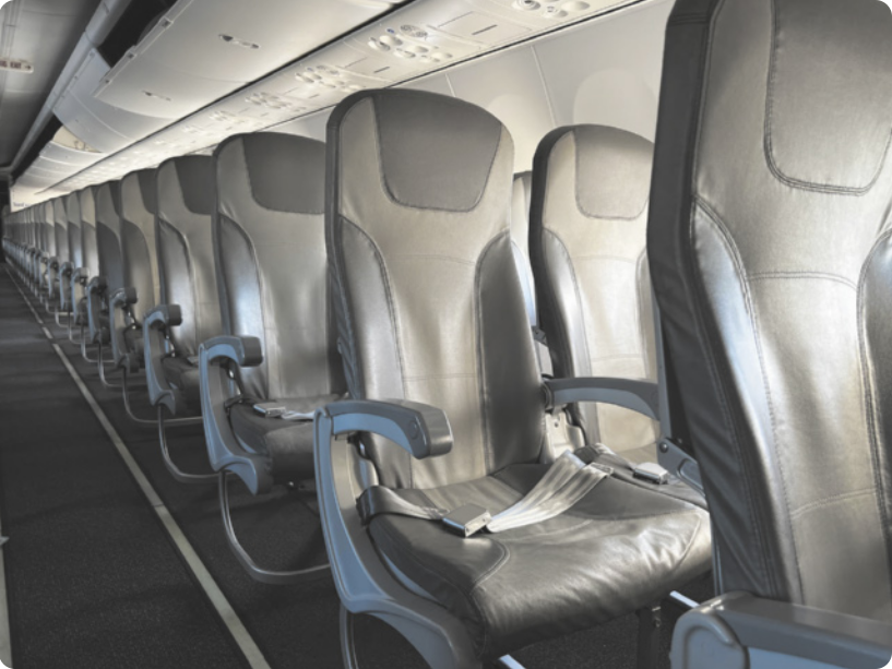 Fotografia do interior de um avião de passageiros vazio, com assentos estreitos e próximos uns dos outros, enfileirados, e com um corredor livre entre as fileiras.