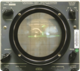 Fotografia de um videogame com a tela de formato circular, com botões e controladores eletrônicos em torno da tela. A tela exibe um círculo e uma linha horizontal luminosos sobre uma quadrícula.