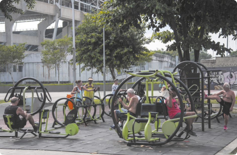 Fotografia de pessoas em uma praça se exercitando em equipamentos de ginástica diversos.