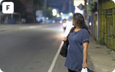 F. Fotografia de uma mulher olhando a rua movimentada de uma cidade, esperando para atravessar, enquanto carrega uma sacola e uma bolsa.