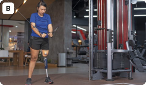 B. Fotografia de uma mulher fazendo exercícios em uma academia. A mulher está usando camiseta e bermuda. Ela usa uma prótese que substitui a sua perna esquerda, e está puxando duas polias enquanto executa um exercício de musculação. Ao fundo, o cenário é de academia, com outros aparelhos em um ambiente fechado.