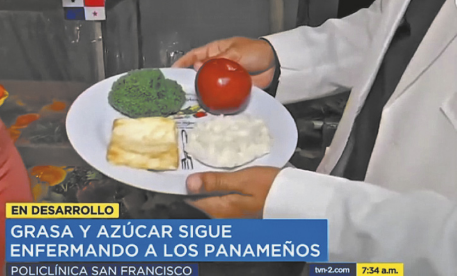 Imagem de uma reportagem de televisão, contendo uma pessoa segurando um prato de comida. O prato contém tomate, brocólis, um pedaço quadrado de algo que se assemelha a queijo, e uma porção de alimento branco, que poderia ser arroz ou purê. Abaixo da foto está escrito: 'En desarollo. Graza y azúcar sigue enfermando a los panameños. Policlínica San Francisco'.