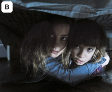 B. Fotografia de uma mulher e uma criança, escondidos embaixo da cama. A mulher é branca e tem os cabelos loiros. Ela abraça um menino que tem os cabelos loiros e franja. Ambos estão olhando para cima com uma expressão de medo.