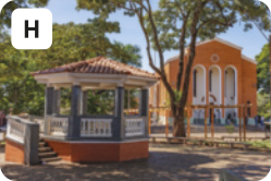 H. Fotografia de um quiosque, algumas árvores e uma igreja ao fundo.
