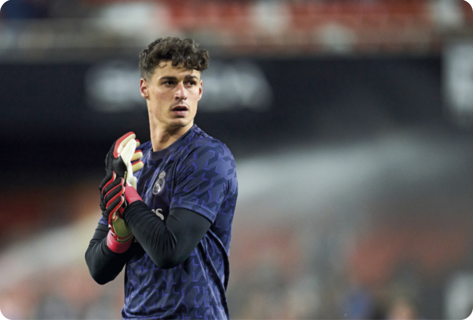 Fotografia de Kepa Arrizabalaga. Ele é branco, tem o cabelo escuro, curto e ondulado, e está usando camisa de futebol com uma camiseta de manga comprida por baixo, e luvas de goleiro. Ele tem a expressão séria e a boca levemente aberta.