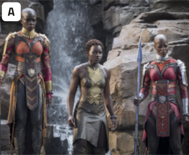 A. Fotografia de três guerreiras negras utilizando trajes típicos da cultura africana retratada no universo de Wakanda, do filme Pantera Negra. As mulheres que estão nas extremidades da fotografia tem o cabelo raspado e usam trajes parecidos, compostos por um tecido justo ao corpo e armaduras nos braços, pescoço e ventre. A mulher da direita segura uma lança. No centro, há uma mulher de cabelos curtos e cacheados, usando trajes mais simples, com padrões geométricos cobrindo o peito e abdômen, e uma saia envolvendo suas pernas, sem armaduras. Ao fundo, há uma cachoeira e rochas de ambos os lados.