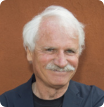 Fotografia de Yann Arthus-Bertrand sorrindo. Ele é branco, tem cabelos e bigode brancos, e está usando camiseta com uma camisa por cima.