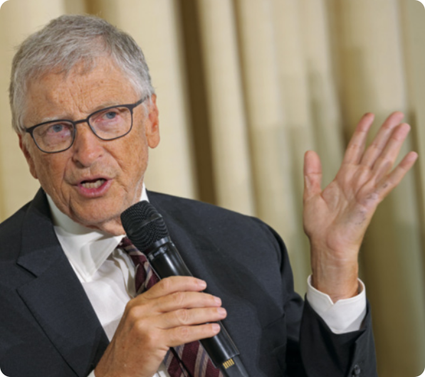 Fotografia de Bill Gates. Ele é branco, tem os cabelos grisalhos, e pele enrugada com sardas. Ele está usando óculos de grau, terno e gravata, e falando a um microfone, enquanto gesticula com uma das mãos. Ao fundo, há uma cortina.