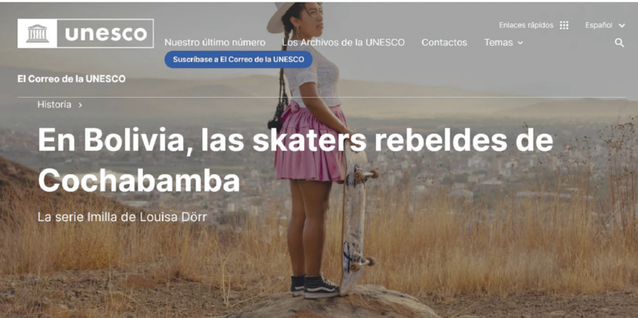 Imagem da página da internet da UNESCO, especificamente da revista online 'El Correo de la UNESCO'. Na manchete está escrito: 'En Bolivia, las skaters rebeldes de Cochabamba' e em letras menores 'La serie Imilla de Louisa Dörr'. Há uma foto de uma jovem em cima de uma pedra em uma paisagem com chão de terra e grama seca, que aparenta ser o alto de uma montanha. Ela está com os cabelos presos por tranças, usando saia rodada, blusa, um chapéu e tênis. Ela segura um skate, olhando para o horizonte. Ao fundo, há vista para uma cidade ou vila.