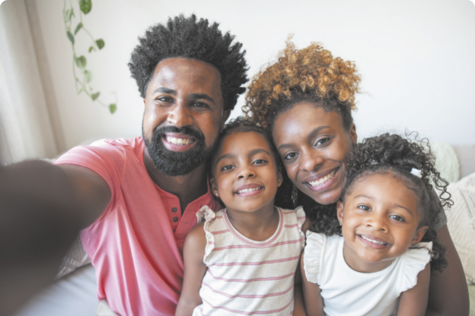 Fotografia de um homem tirando uma fotografia em família. Na imagem um homem, uma mulher e duas crianças, abraçados.