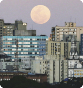 Fotografia de paisagem urbana com diversos edifícios. A Lua aparece Cheia no céu, acima deles.