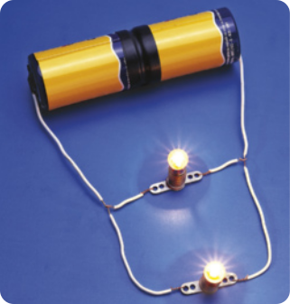 Fotografia de um resistor cilíndrico, na posição horizontal, com um fio saindo de cada lado, ligados a duas lâmpadas paralelas, acesas.
