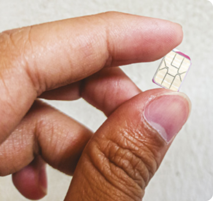 Fotografia de um nano chip sendo segurado por uma pessoa. O chip de metal é um pequeno retângulo, plano e tem linhas de circuitos no interior. Está entre os dedos polegar e indicador da mão de uma pessoa.